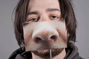 Person holding a photo of a nose aligned with their face creating an amusing effect