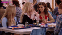 Personajes de la serie Mean Girls en la cafetería, chocando las manos en un gesto de complicidad