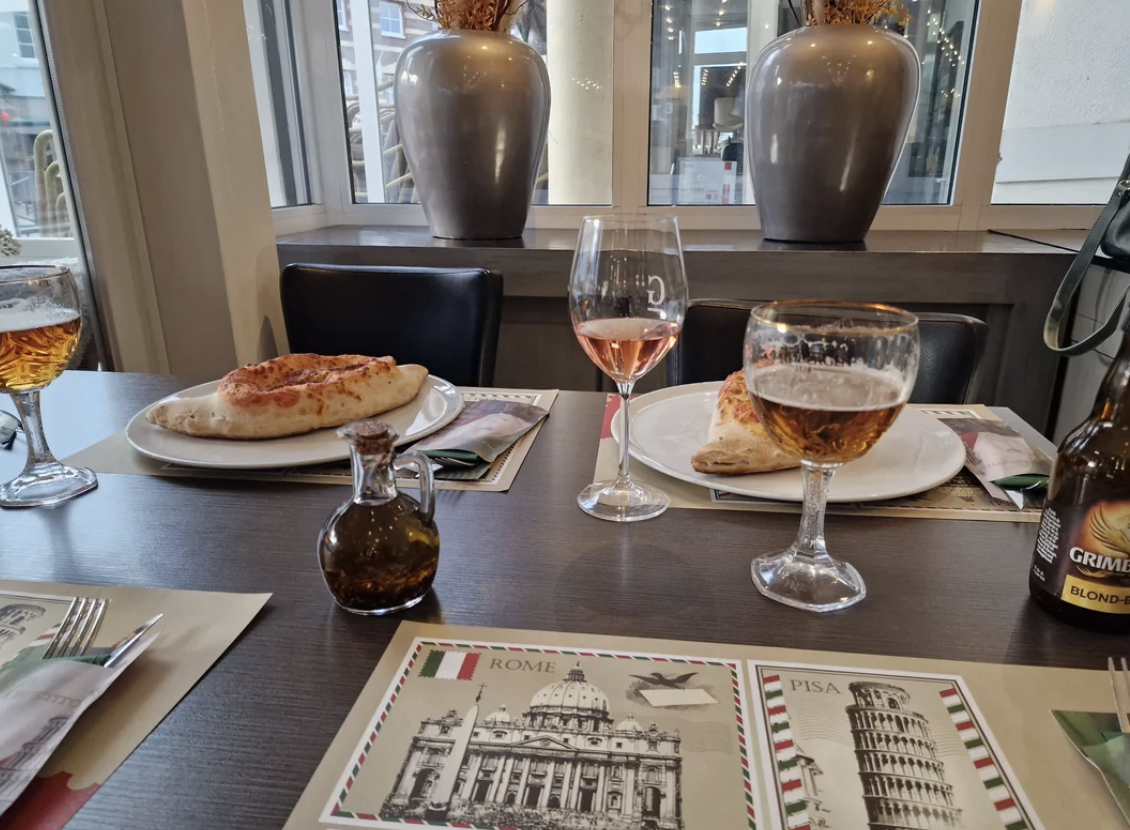 Two glasses of beverage with a pizza on a table, menus featuring Italian landmarks are visible