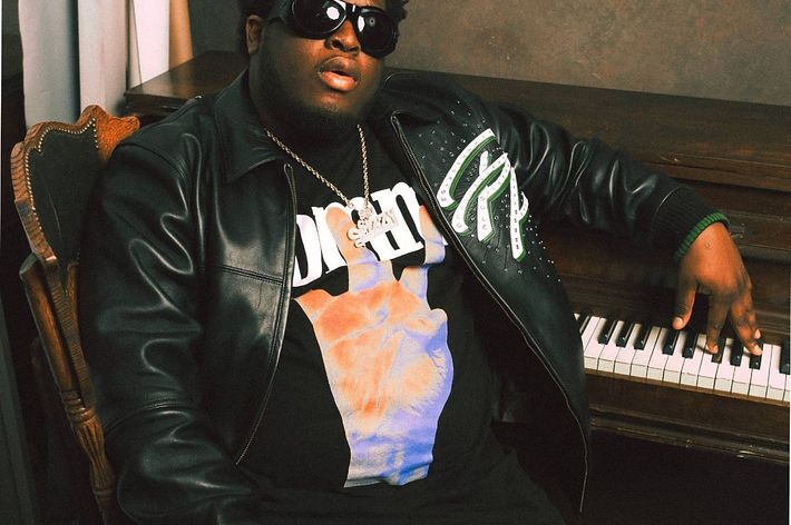 Musician in a leather jacket and sunglasses sits beside a piano, exuding a relaxed vibe