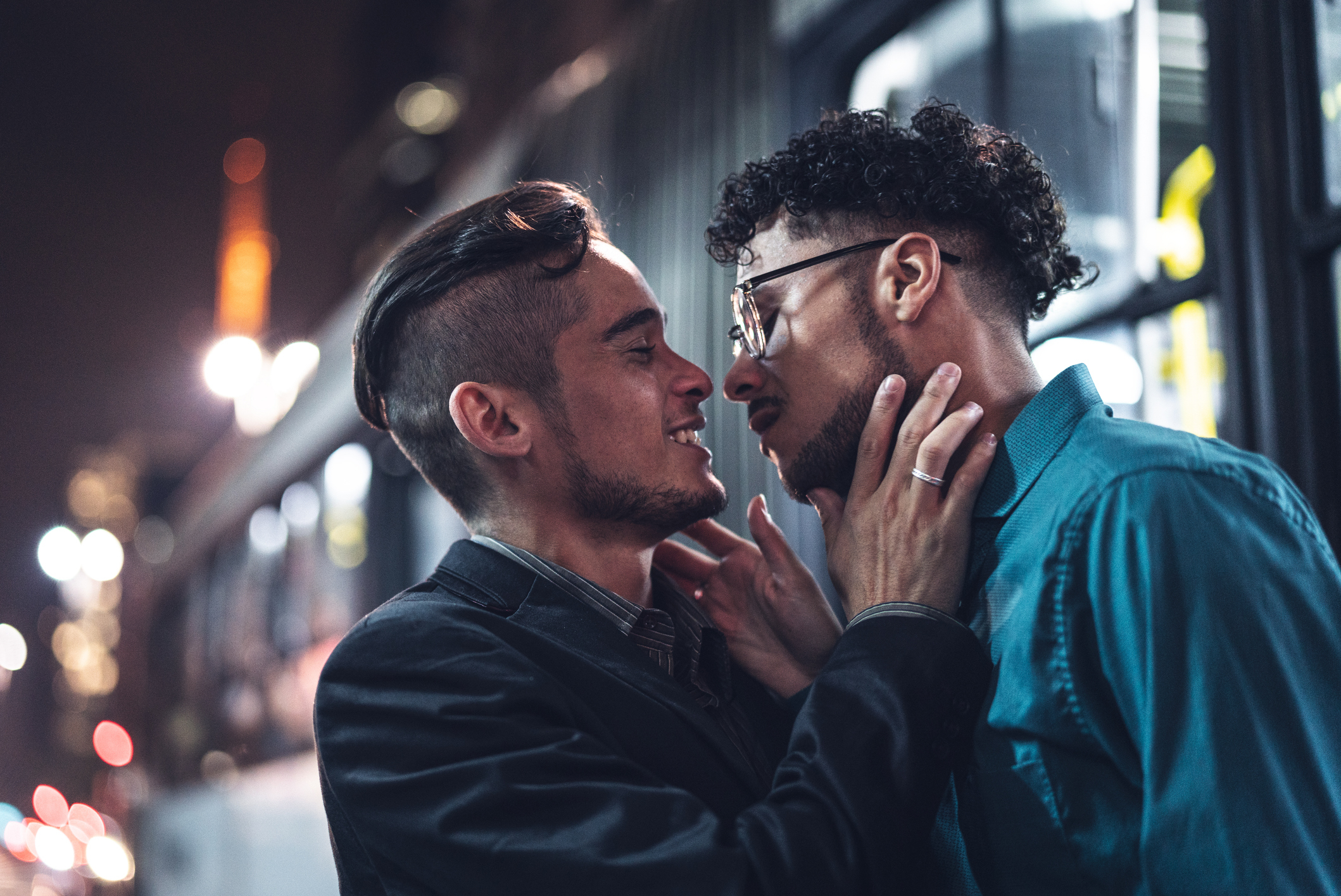 Two people embracing and touching foreheads affectionately at night, with city lights in the background