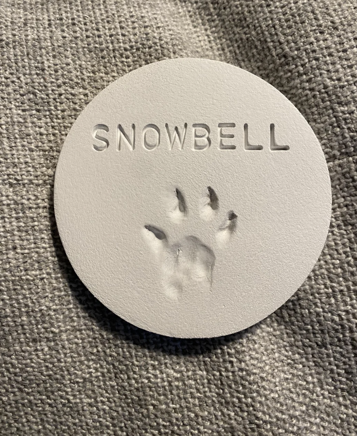 Circular object with raised paw print and &quot;SNOWBELL&quot; text, suggesting a pet keepsake