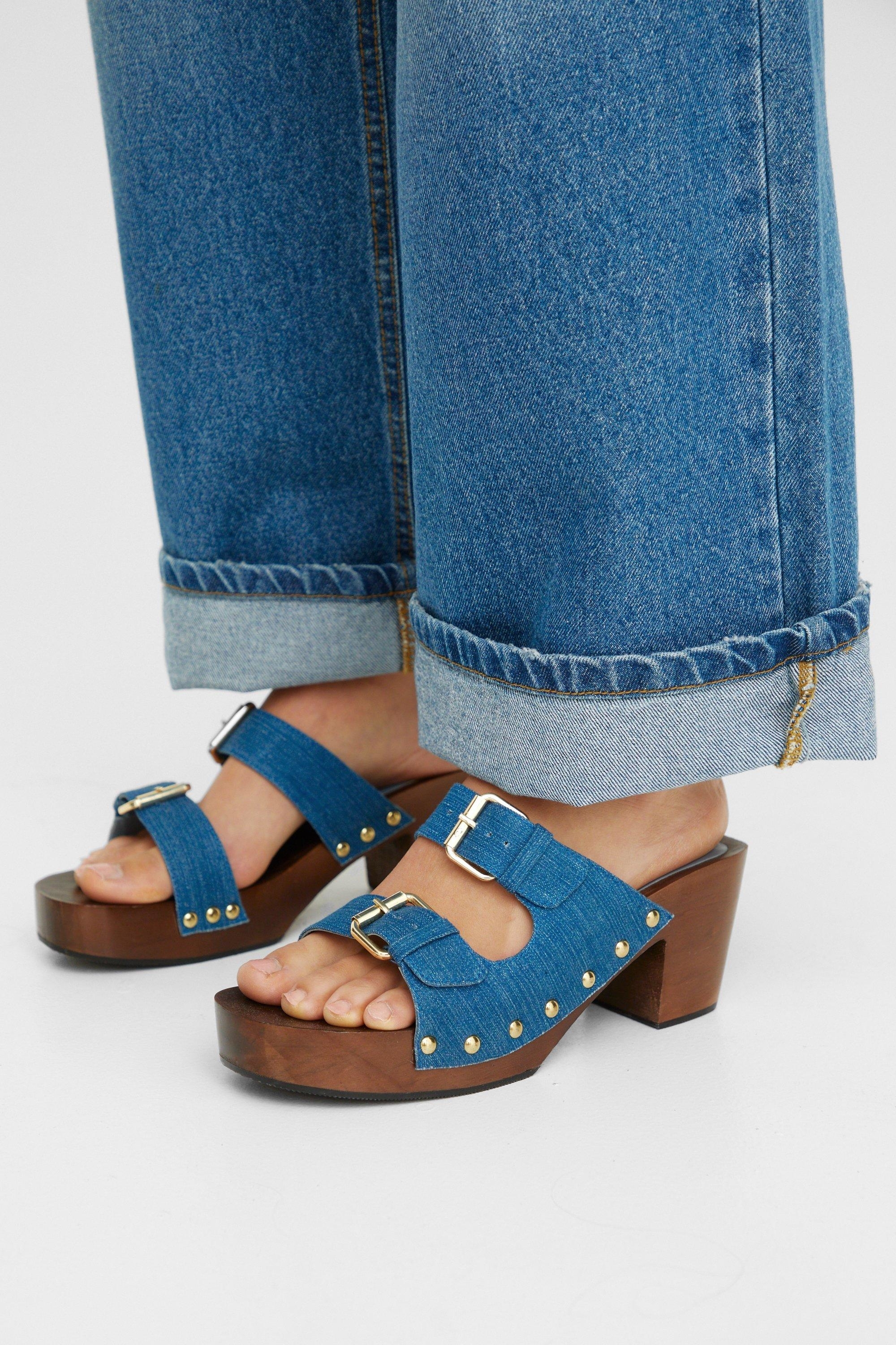 Person wearing blue jeans and brown heeled sandals with buckle details