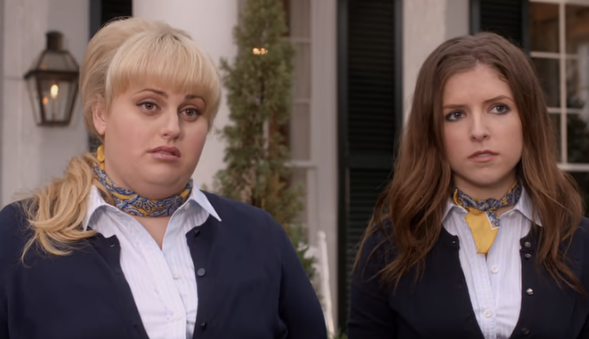 Fat Amy and Beca, played by Anna Kendrick, stand side by side in their matching uniforms, looking serious