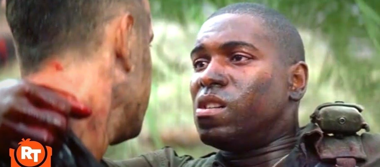 Two men in military gear face each other, one with blood on his face, in a tense moment