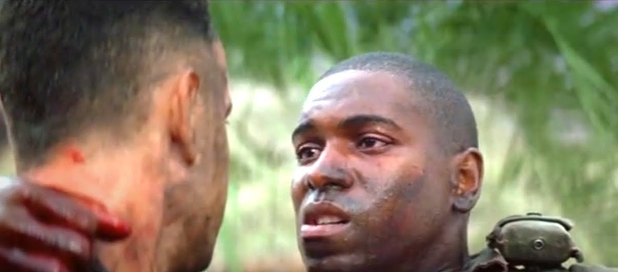 Two men in military gear face each other, one with blood on his face, in a tense moment