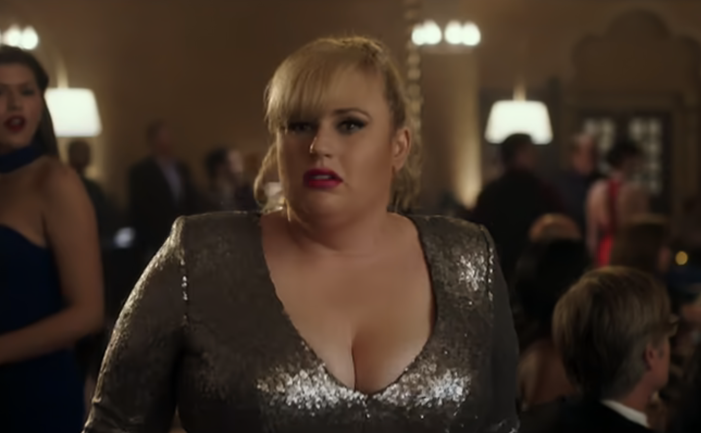 Rebel Wilson in a glittery V-neck dress at a formal event, looking surprised