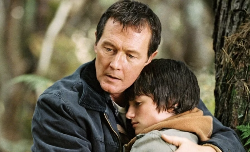 Two actors portraying a father and son sharing an emotional embrace in a forest setting