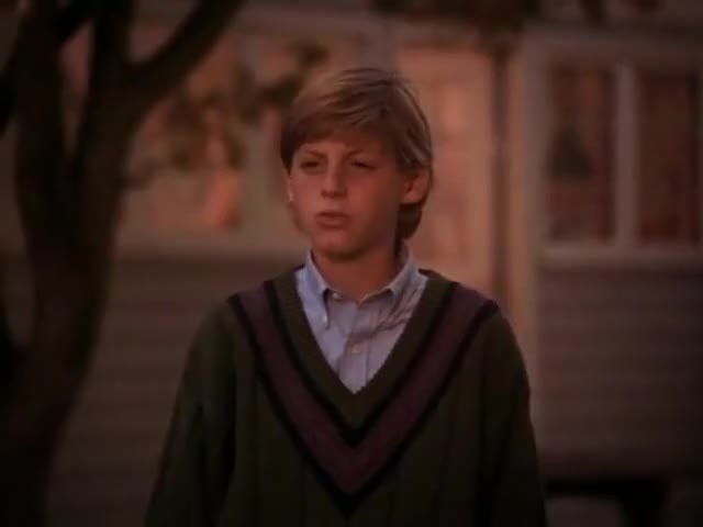 Young boy in a sweater over a collared shirt, appearing in a TV show scene