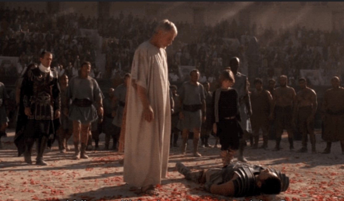 Scene from a film with a man in a Roman robe standing over another lying in an arena
