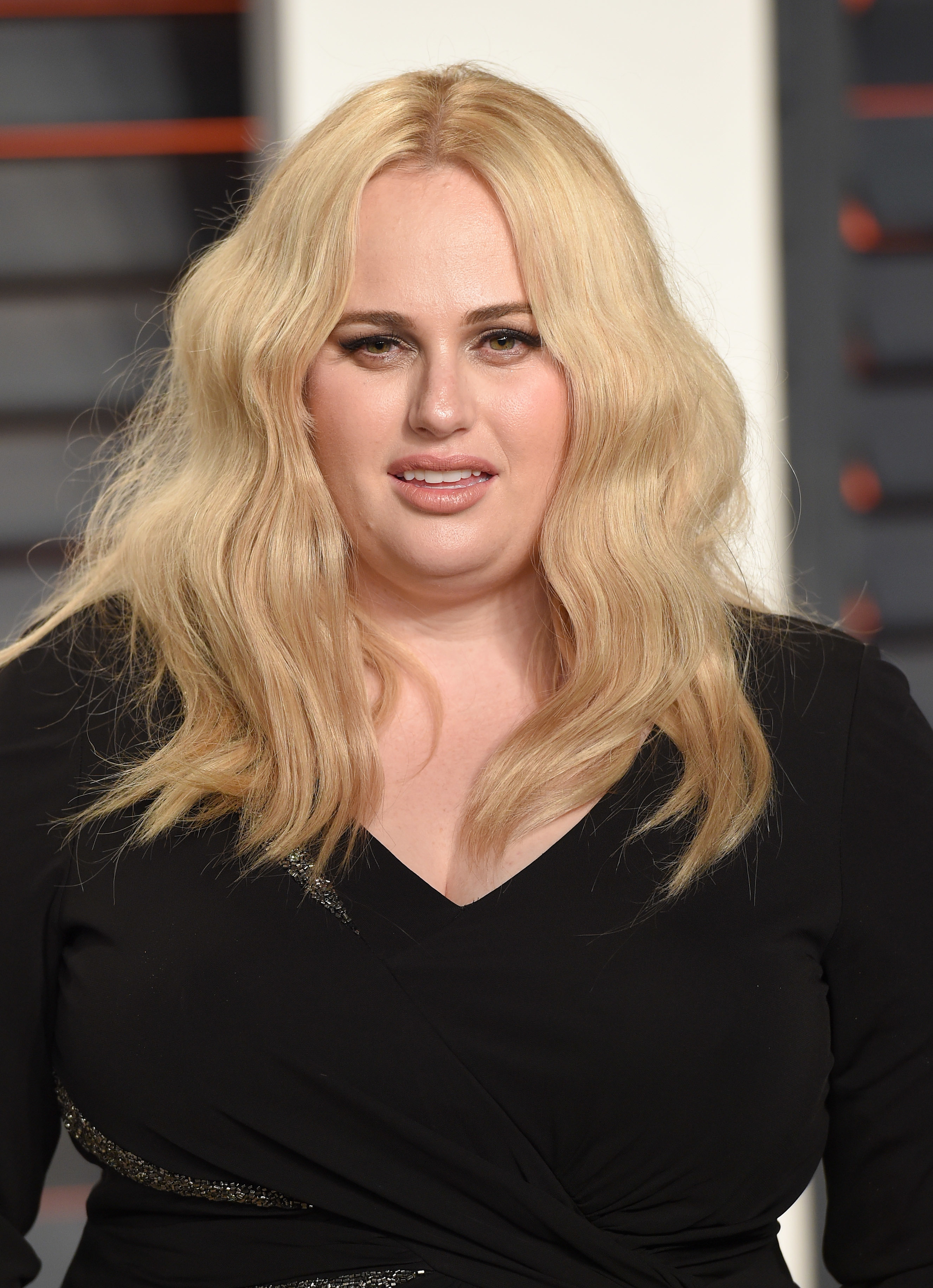 Rebel Wilson in a dress with a v-neckline and sparkle detail, posing at an event