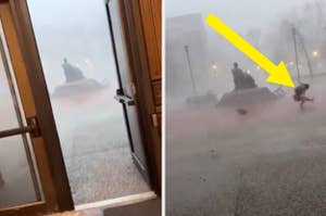 A person struggles against strong winds and rain during a storm, almost blown away while passing a statue