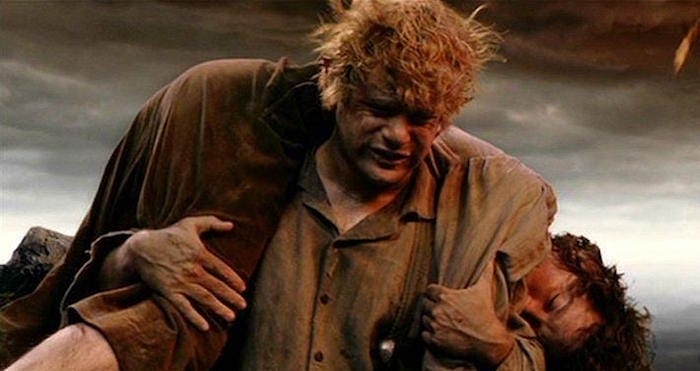 Samwise Gamgee carrying an exhausted Frodo Baggins in a rugged terrain