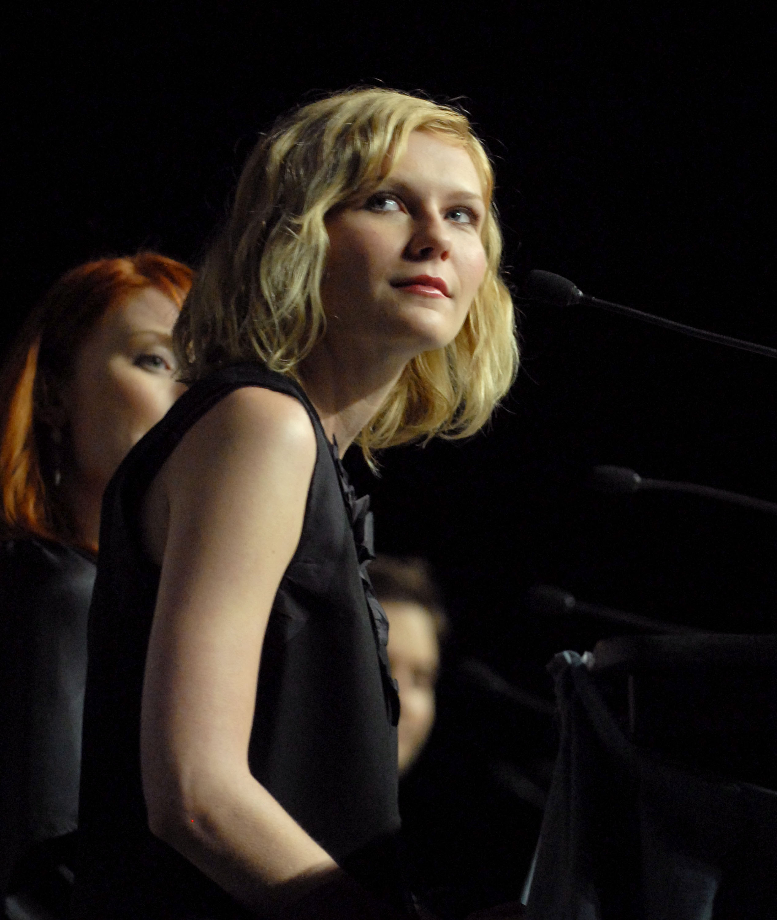 Kirsten Dunst in a sleeveless top speaks at a podium