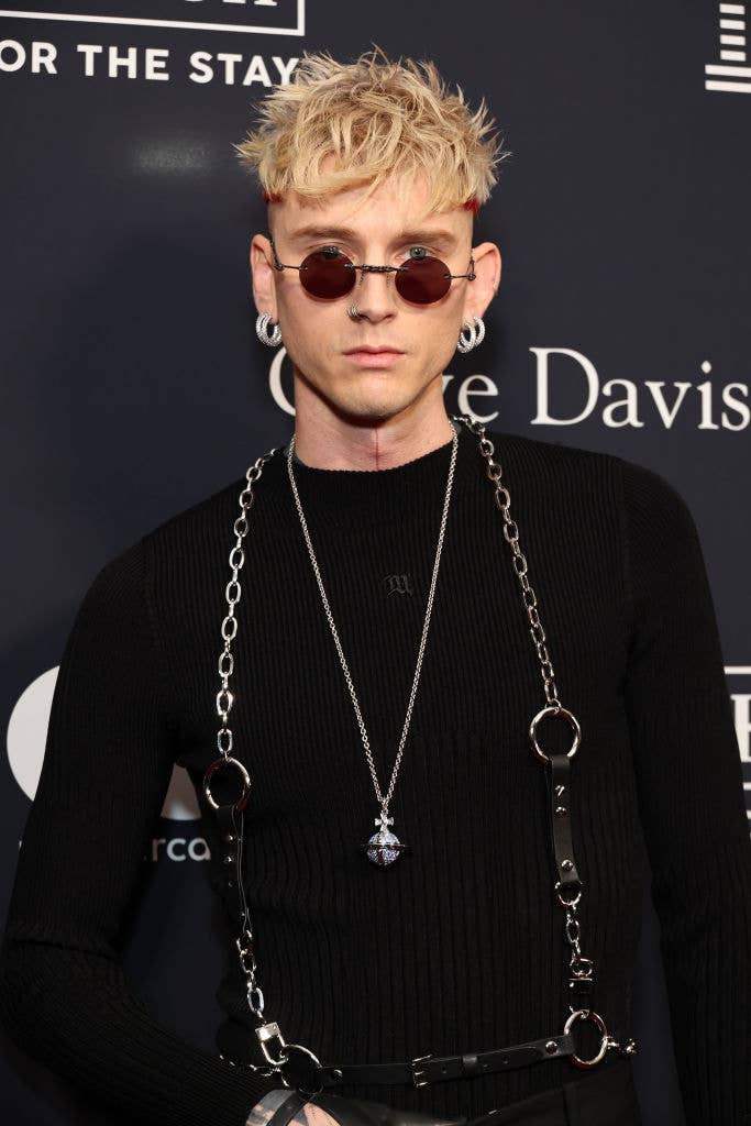 Person in black outfit and sunglasses with chain accessories stands against backdrop with text