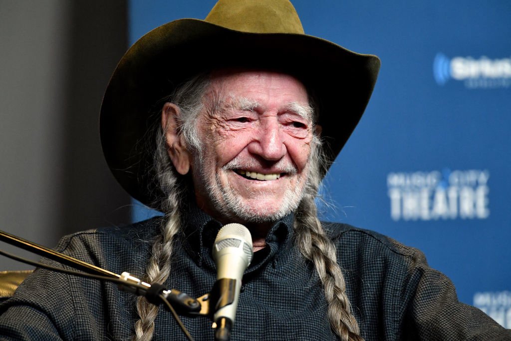 Willie Nelson smiling in a cowboy hat and braids at an event