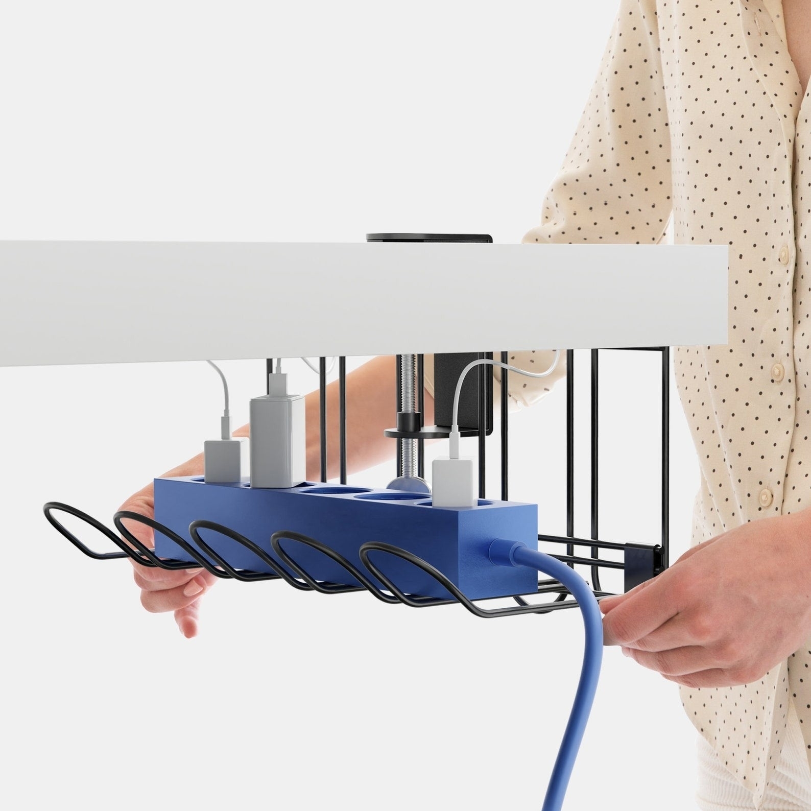 Person adjusting under-desk cable management tray with surge protector on it