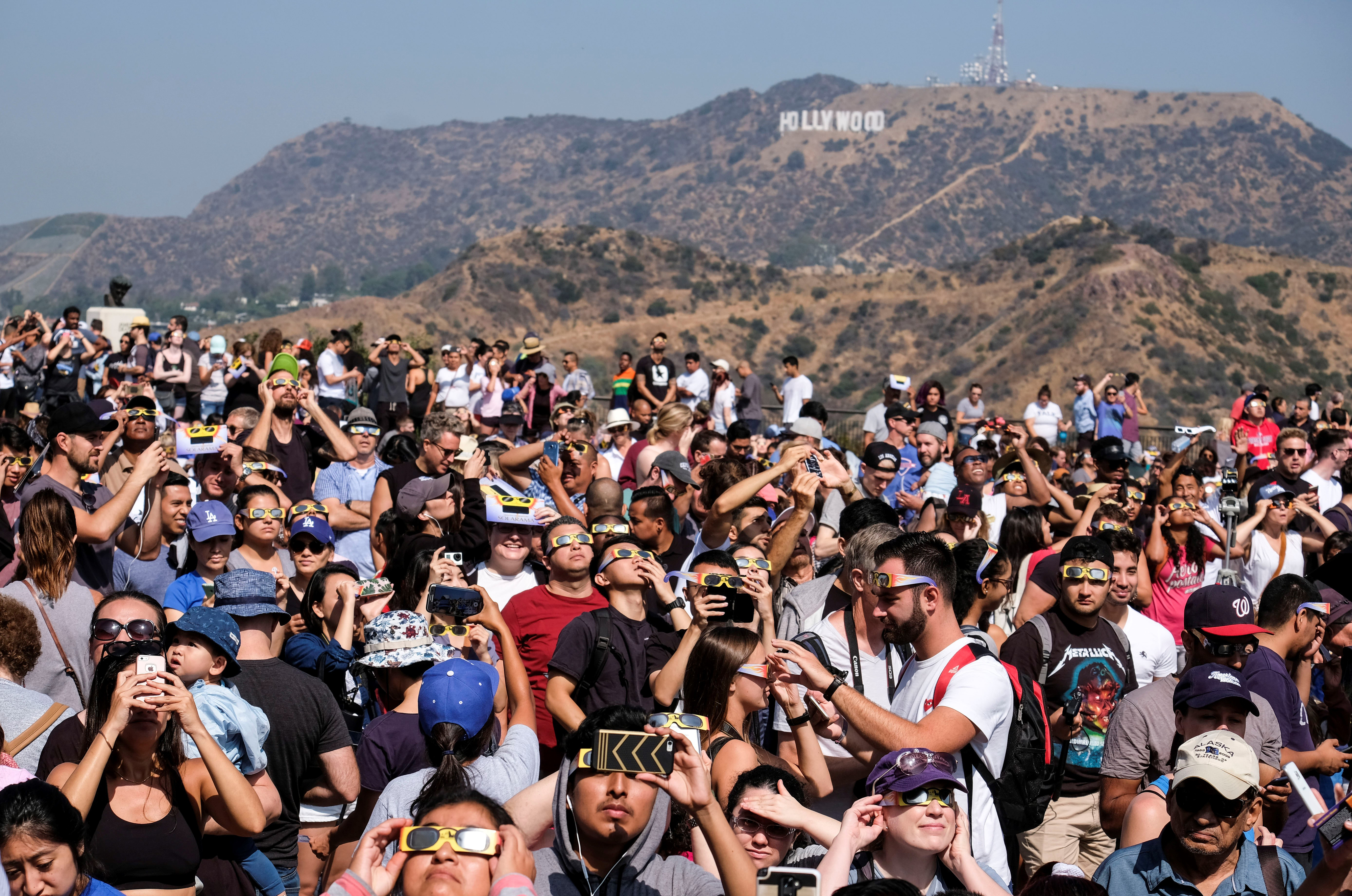 Crowd with eclipse glasses looking upwards near Hollywood sign