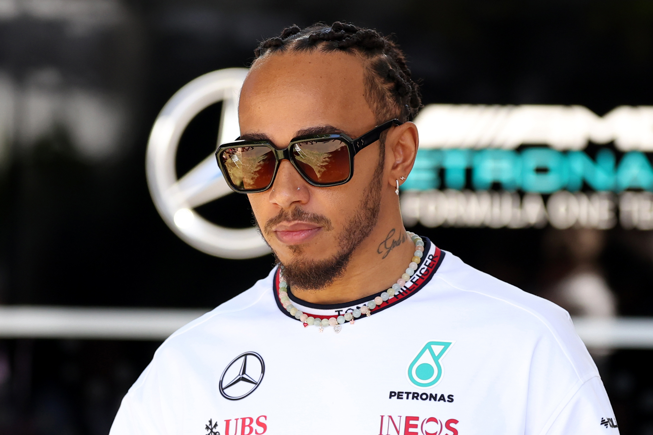 Lewis Hamilton in a white team jersey with sponsor logos, wearing sunglasses