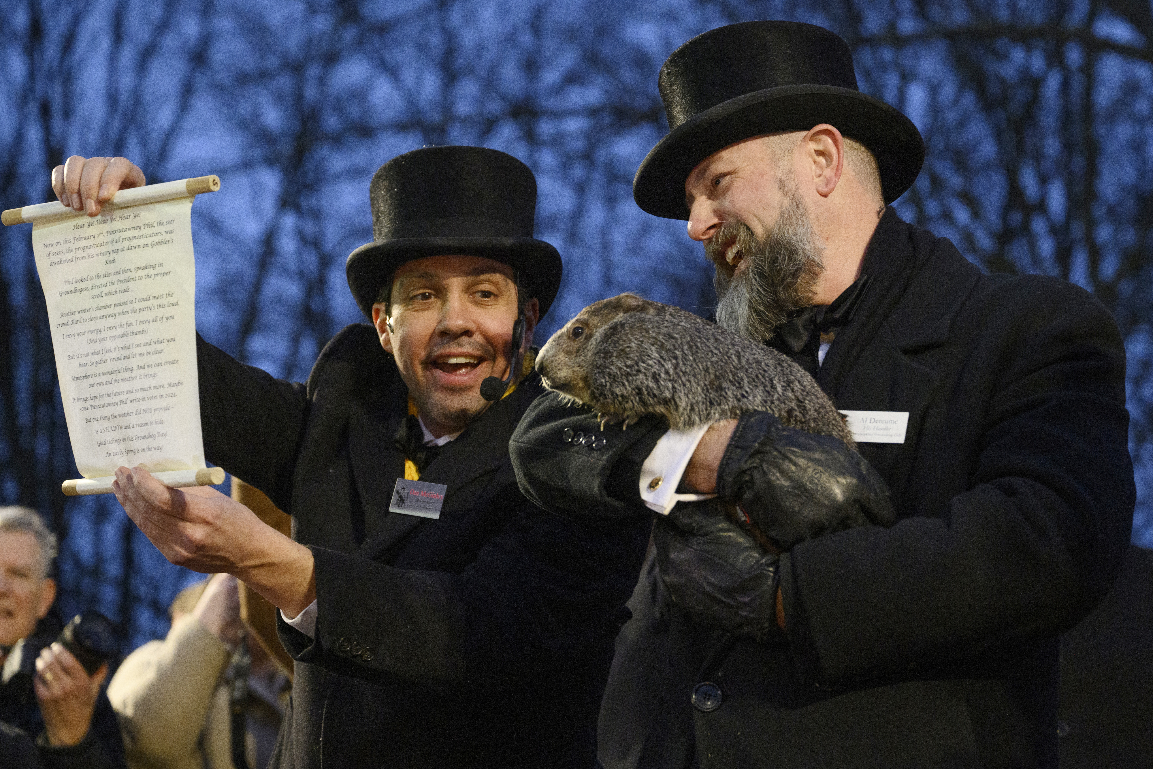 Two men in top hats hold a groundhog and a proclamation at a Groundhog Day event
