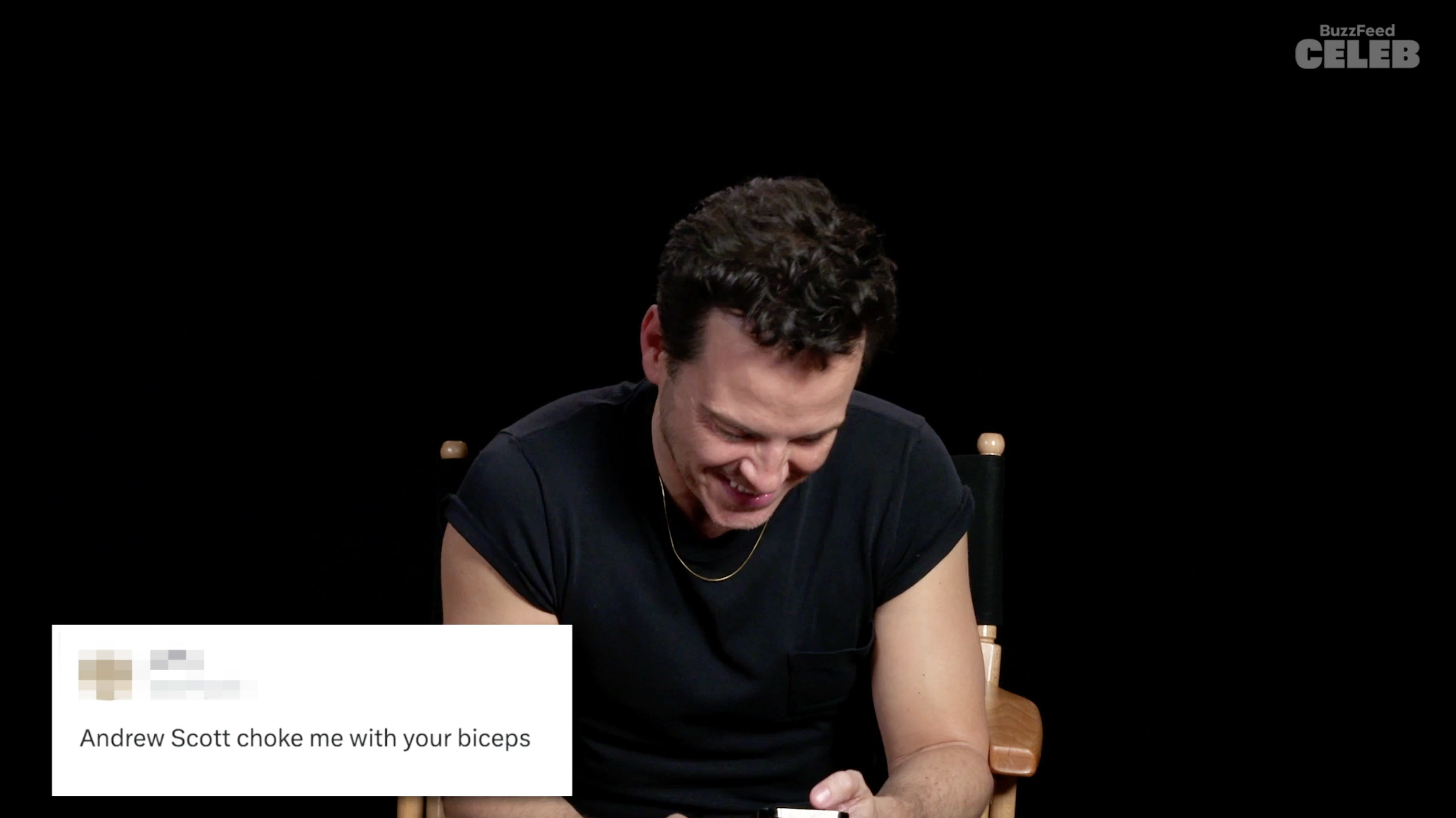 Andrew Scott smiles and looks down, seated before a screen displaying a playful message from a fan