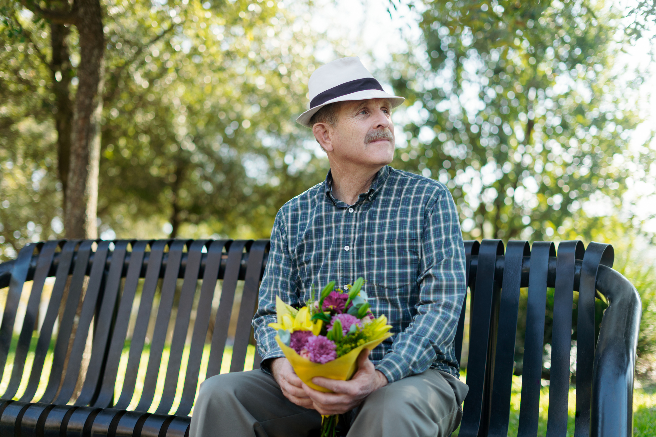 Elderly man seated on park bench holding bouquet, looking hopeful