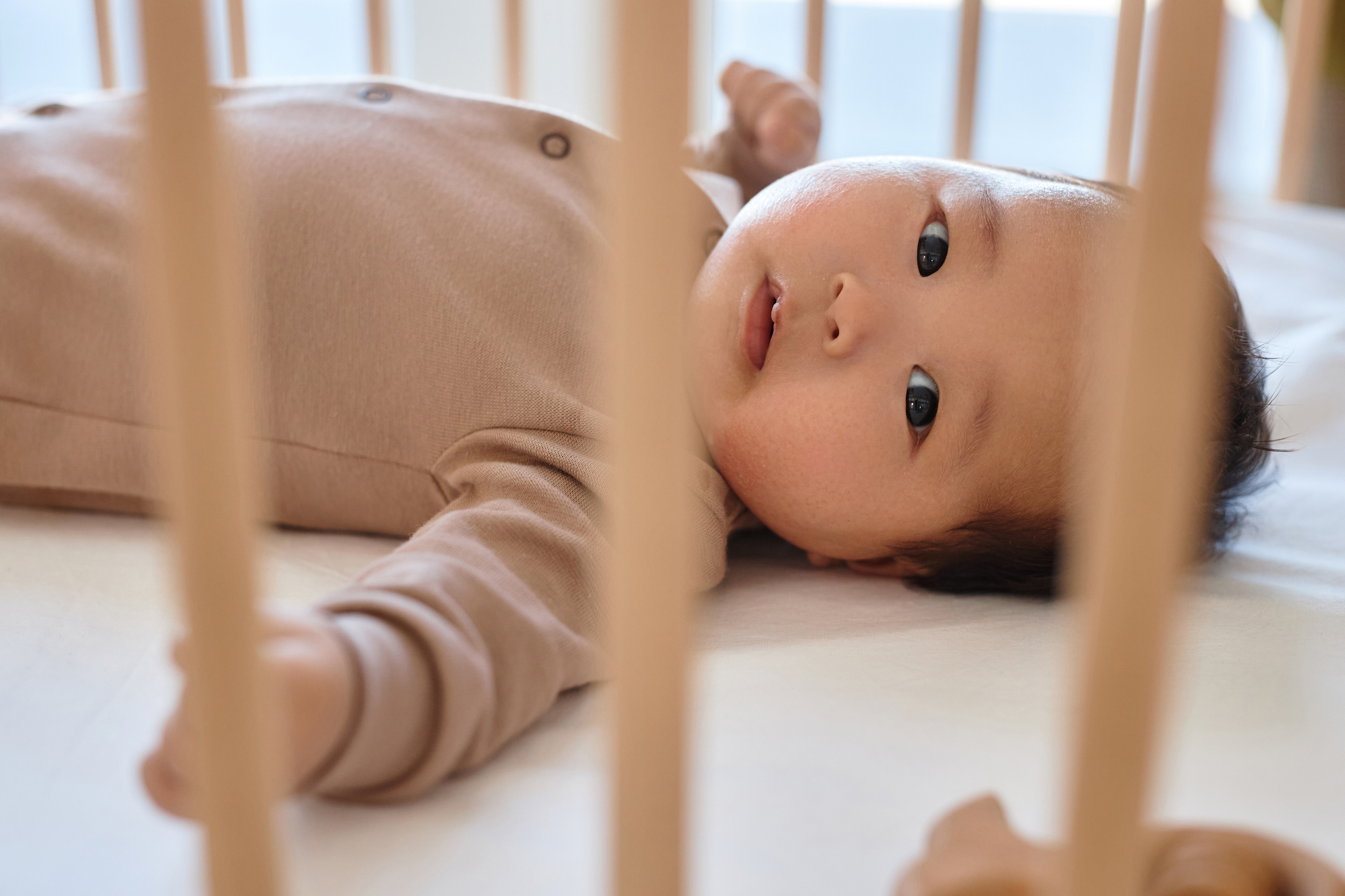 Infant lying in a crib looking towards the camera, image evokes themes of early childhood and nurturing