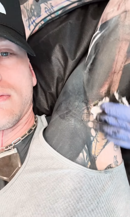 Person getting a tattoo on arm, artist in focus, wearing gloves, ink visible