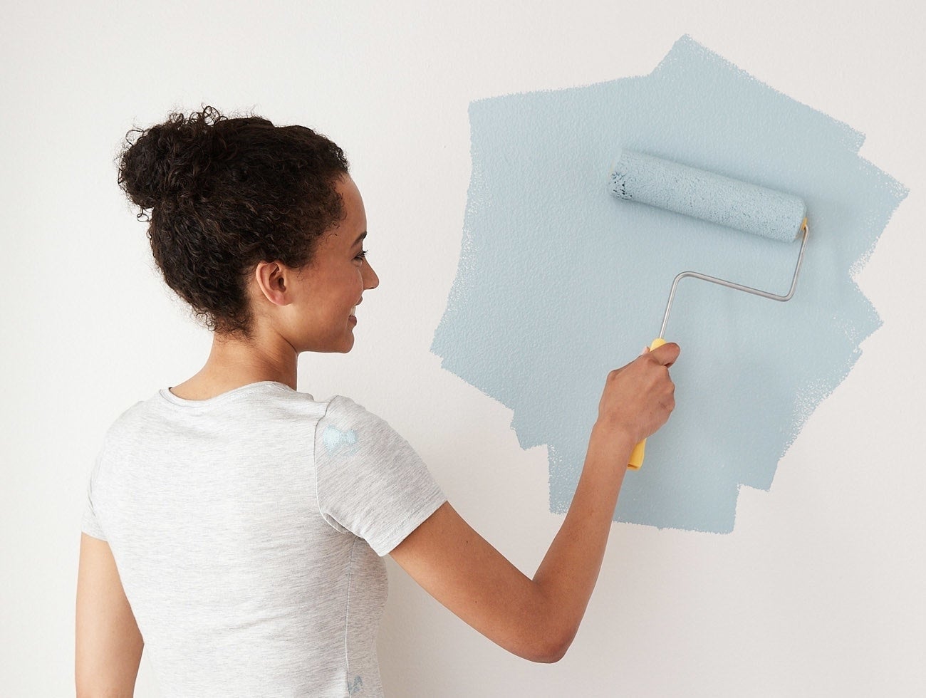 Woman painting a wall with a roller, mid-application, wearing a casual white shirt