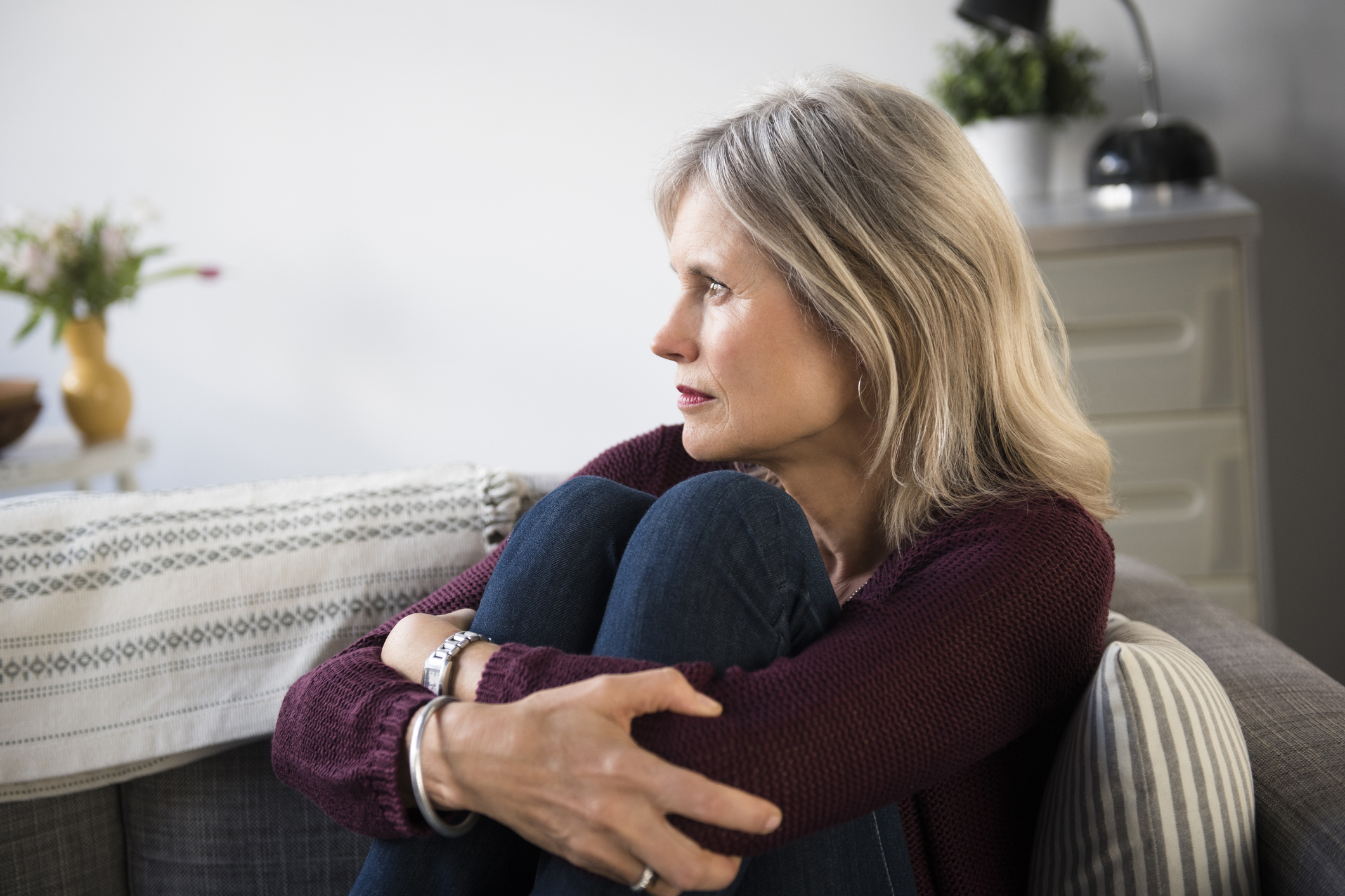Woman sitting on couch looking thoughtful with arms wrapped around her knees
