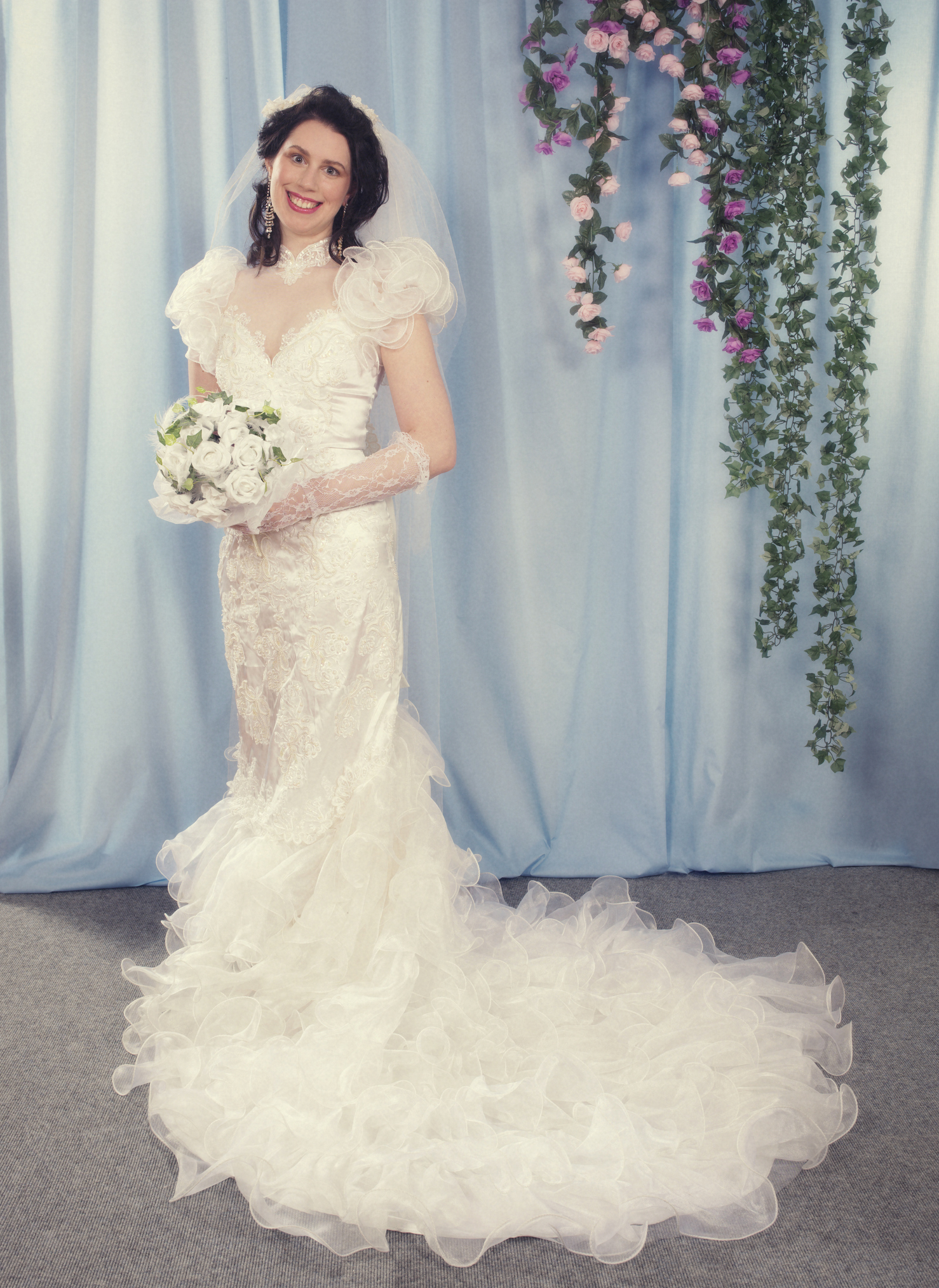 Woman in an embellished wedding dress with voluminous sleeves and a flowing train holds a bouquet