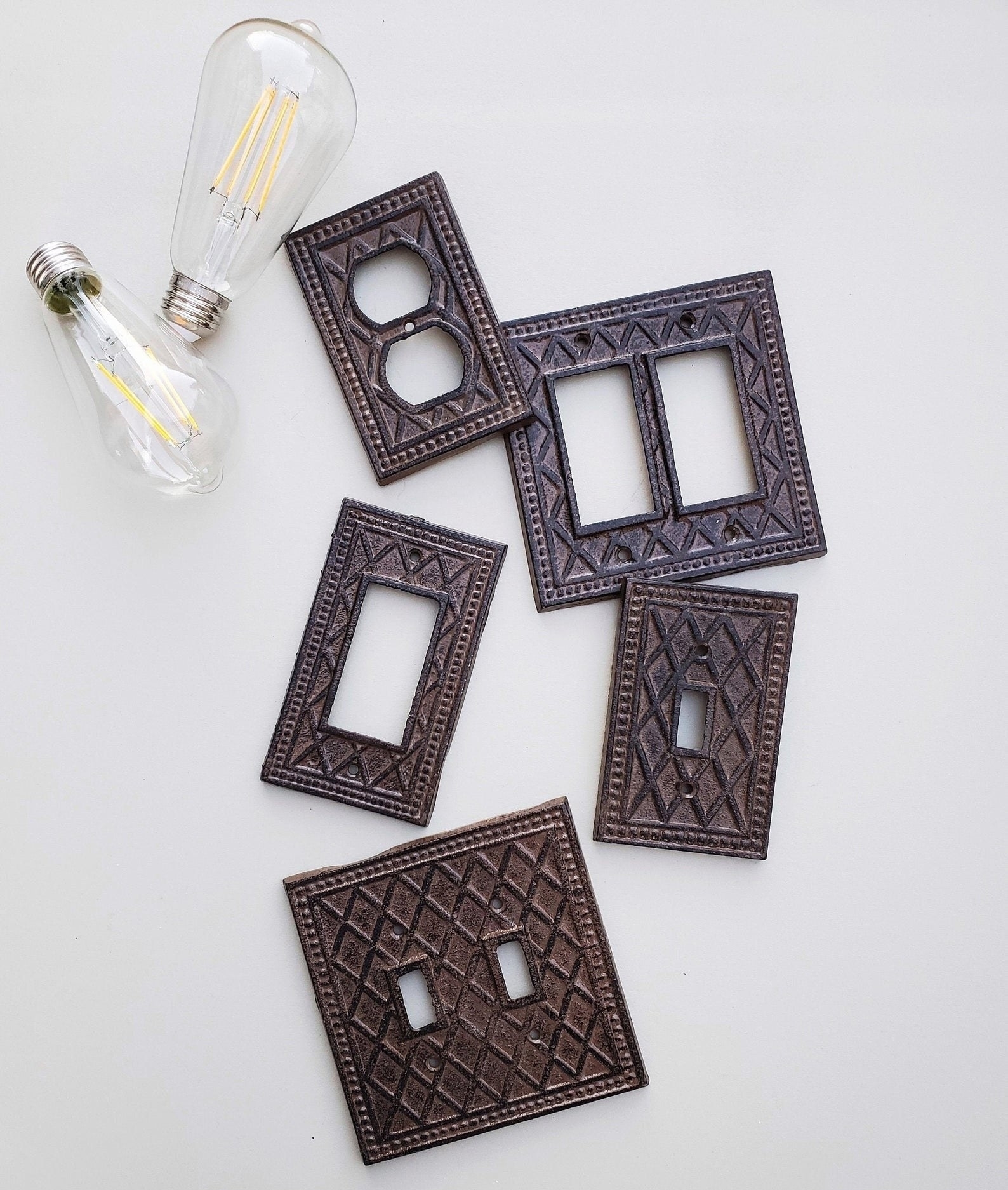 An assortment of decorative light switch covers next to a light bulb on a flat surface