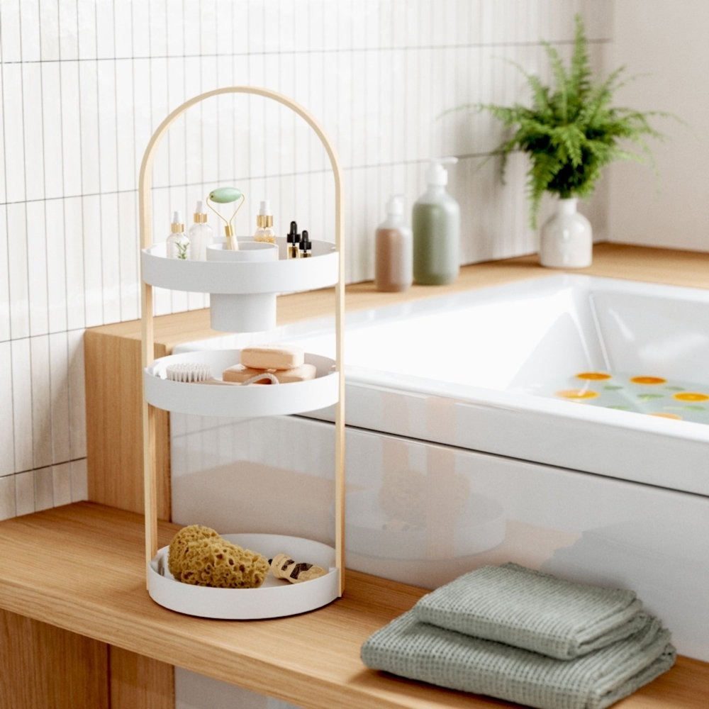 Three-tiered bathroom storage stand with various toiletries and towels next to a sink