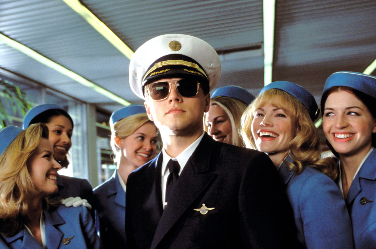 Man in pilot uniform surrounded by smiling flight attendants in blue attire