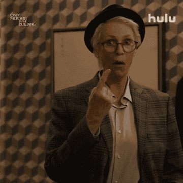 Woman in a suit and hat gesturing number one with her finger