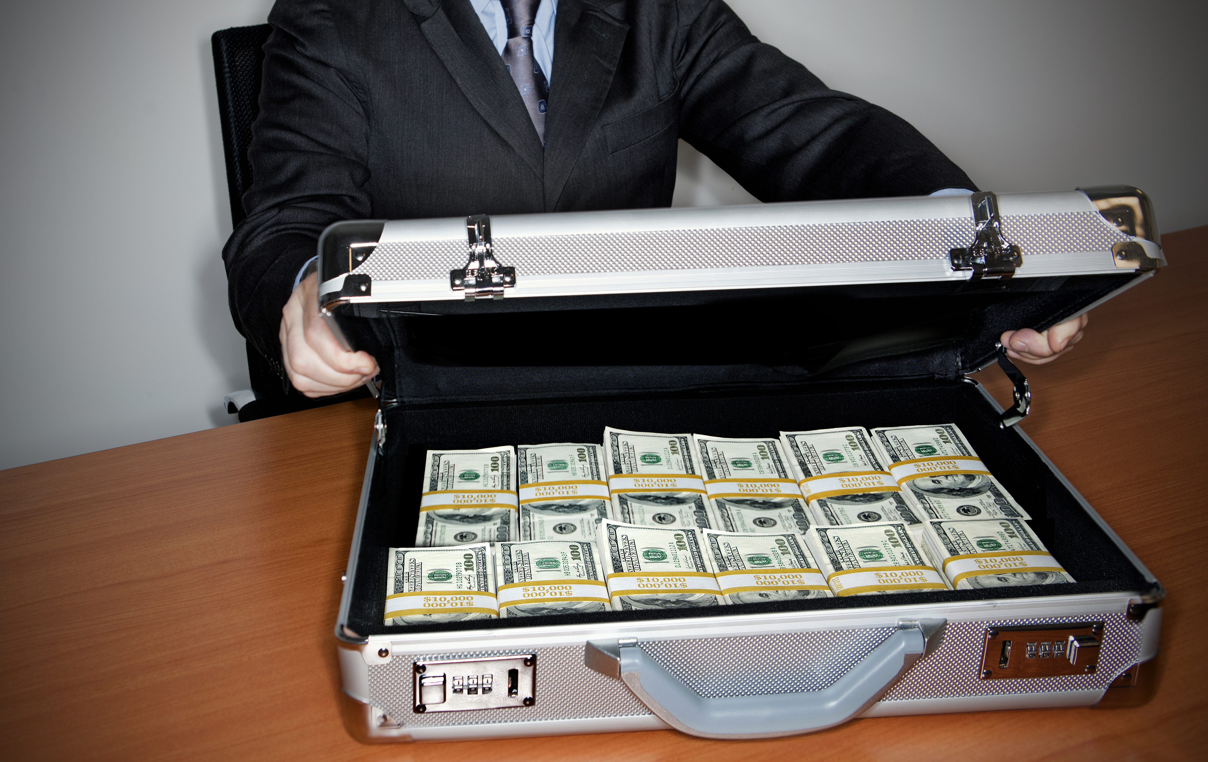 Person opening suitcase full of cash on a table, suggesting expensive travel or opulent lifestyle