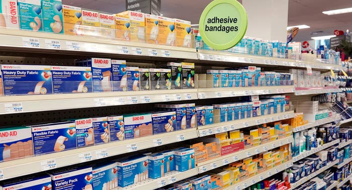 Shelves stocked with various boxes of adhesive bandages in a store aisle under a sign that says &quot;adhesive bandages&quot;
