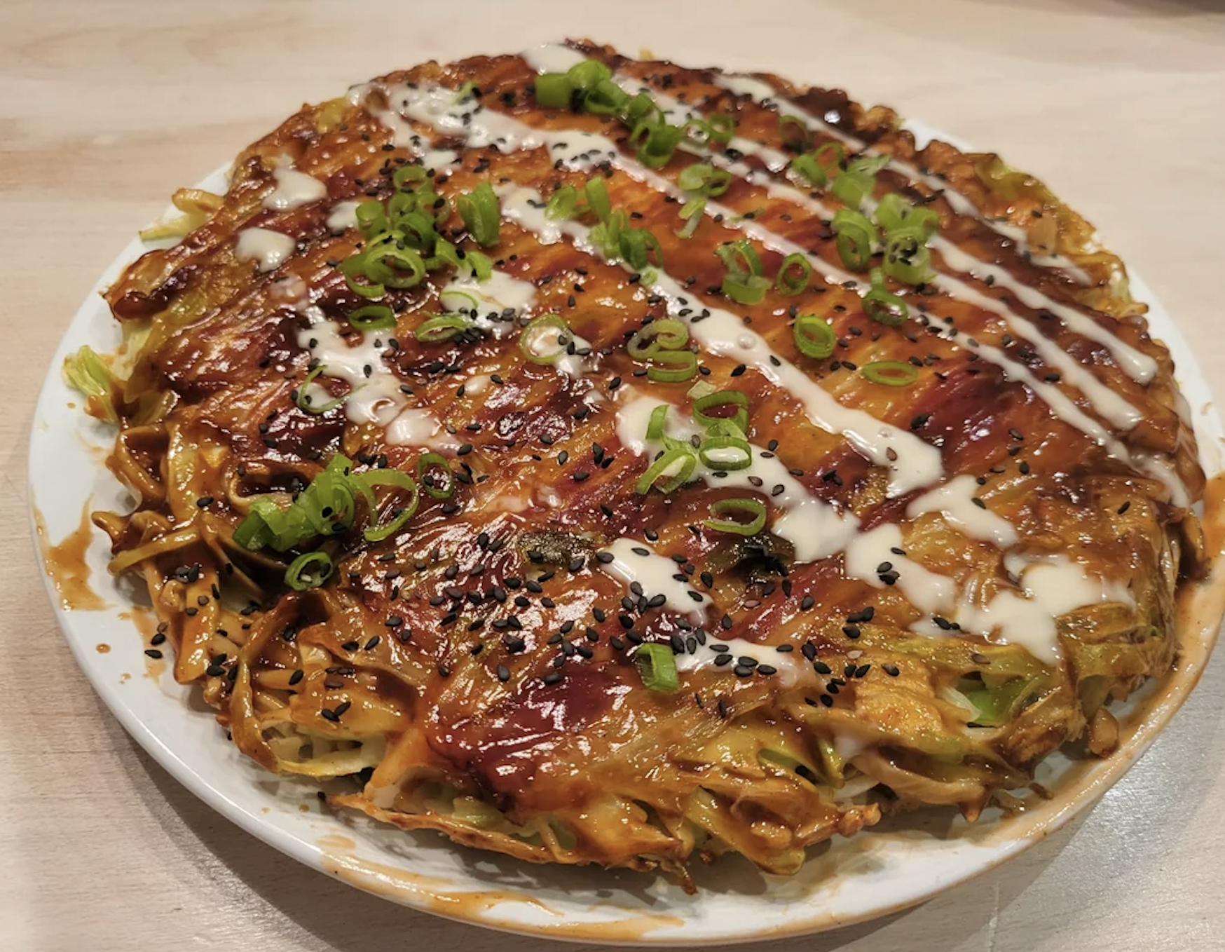 Okonomiyaki (Japanese savory pancake) topped with sauces, green onions, and sesame seeds on a plate