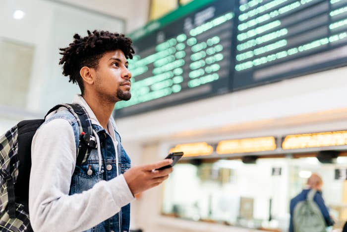 Man with backpack holding phone, looking at airport departure board
