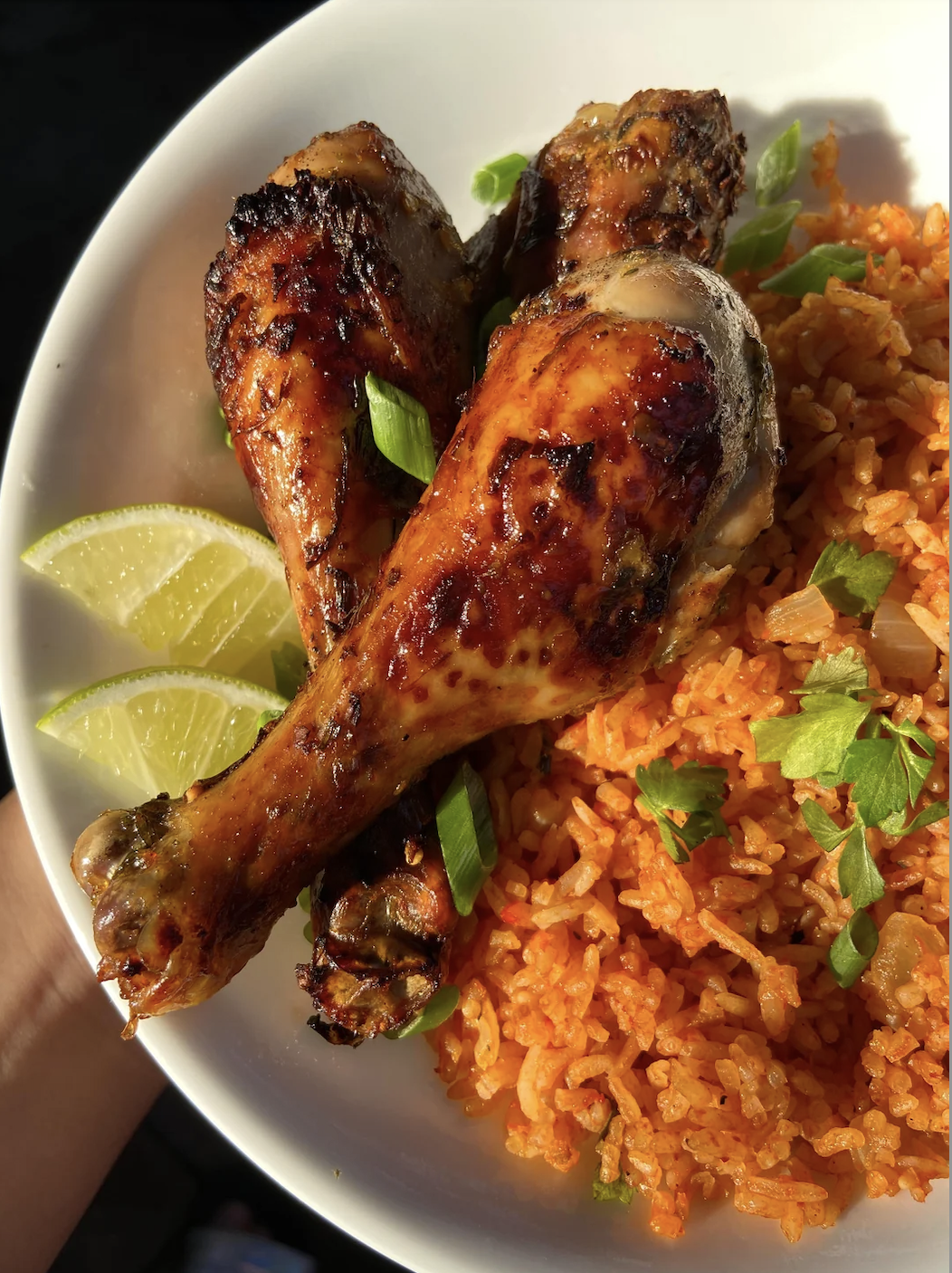 Grilled chicken drumsticks on a bed of seasoned rice with lime wedges and parsley garnish