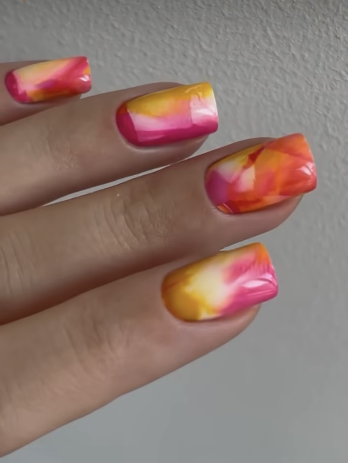 Close-up of a hand with nails featuring a marbled design in shades of pink and yellow
