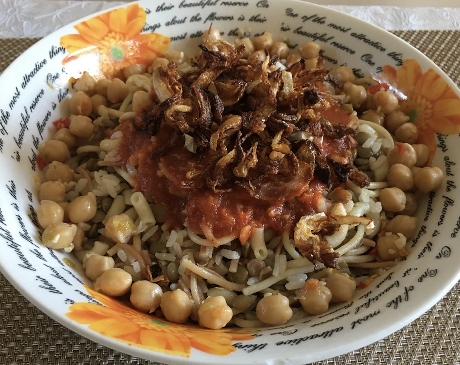 A plate of koshari with lentils, rice, pasta, chickpeas, tomato sauce, and fried onions
