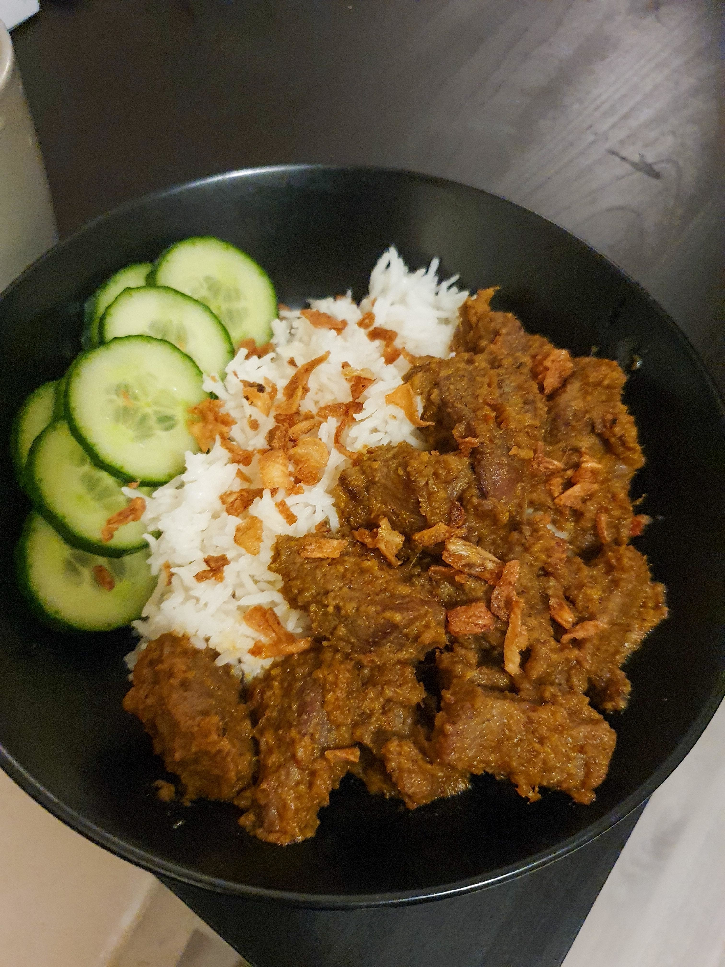Plate of rice with beef rendang and sliced cucumbers