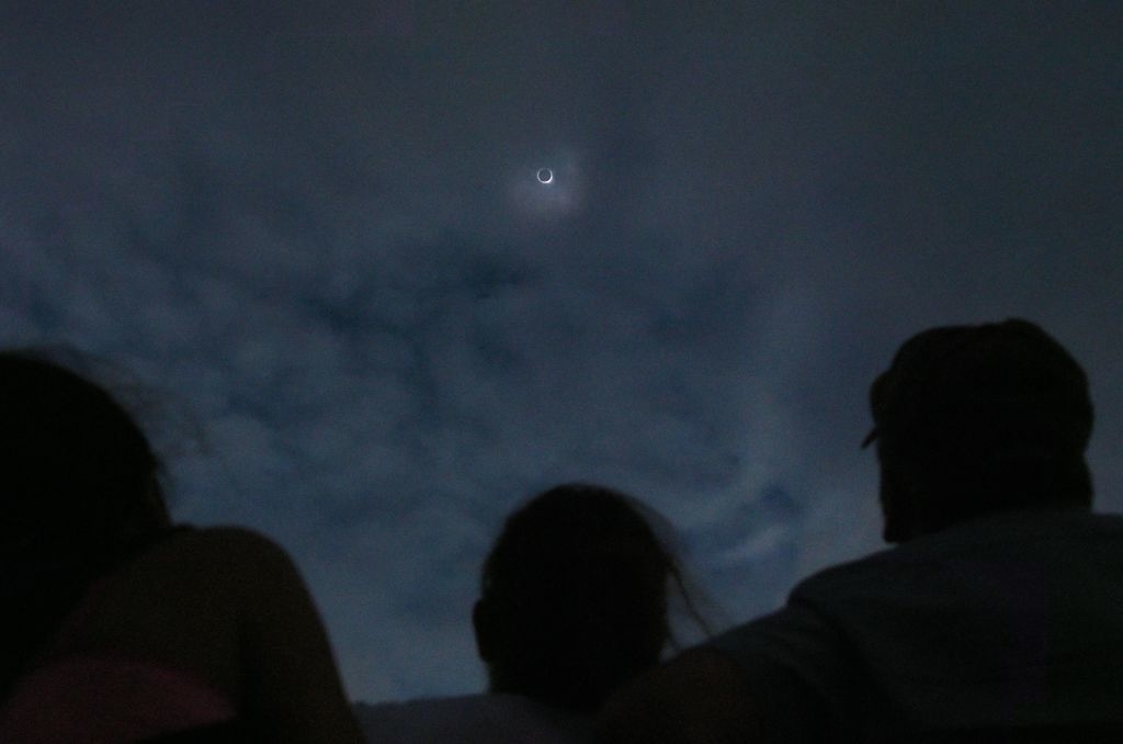 Two people observing a night sky with visible clouds and a bright crescent moon