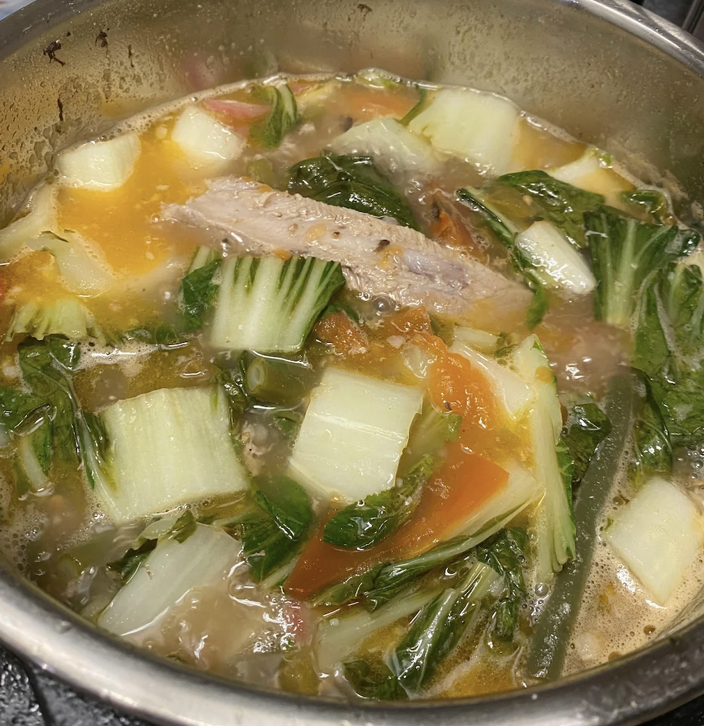A pot of soup with vegetables and meat simmering on the stove
