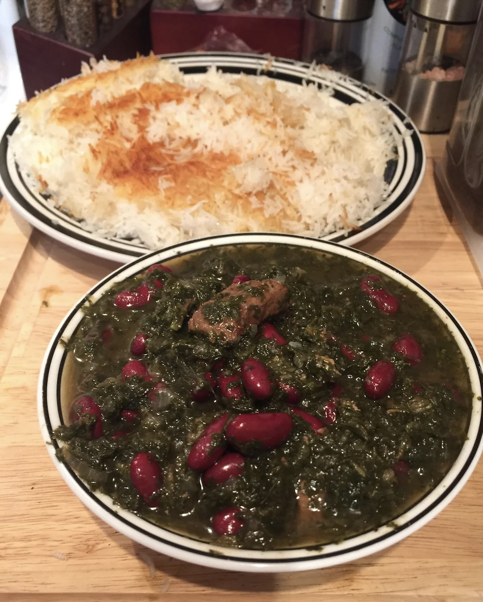A bowl of spinach and meat stew with kidney beans next to a bowl of Persian rice