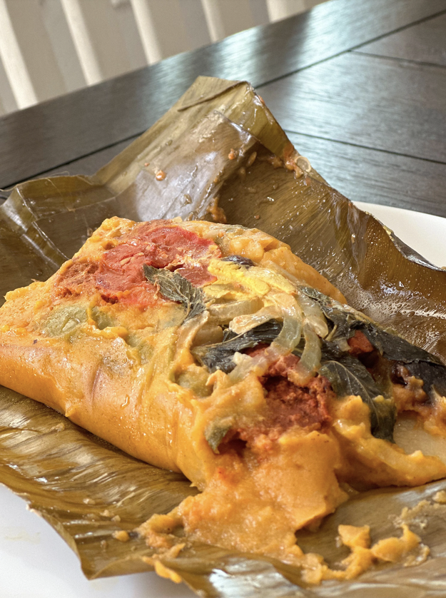 Traditional tamale unwrapped and partially eaten on a white plate