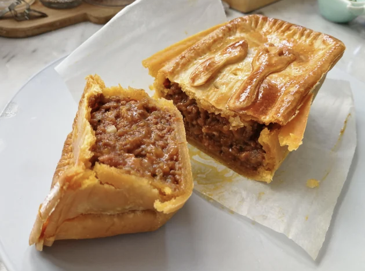 A meat pie cut open to reveal the filling, with one half leaning against the other