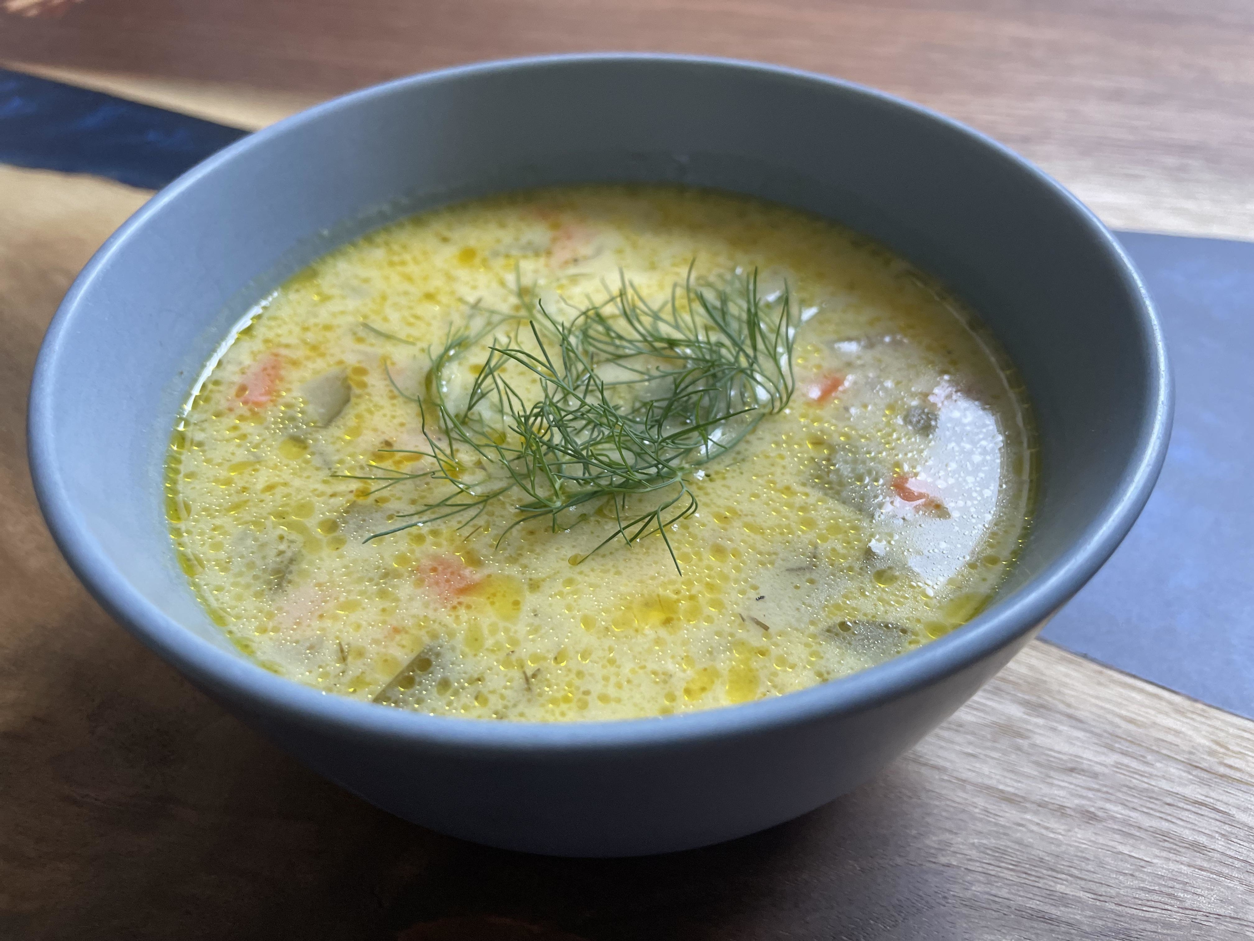 A bowl of soup with vegetables and a garnish of fresh dill on top