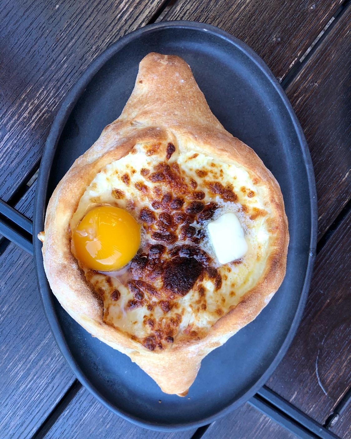 Georgian cheese bread, khachapuri, with an egg in the center and a pat of butter on top, served on a black plate